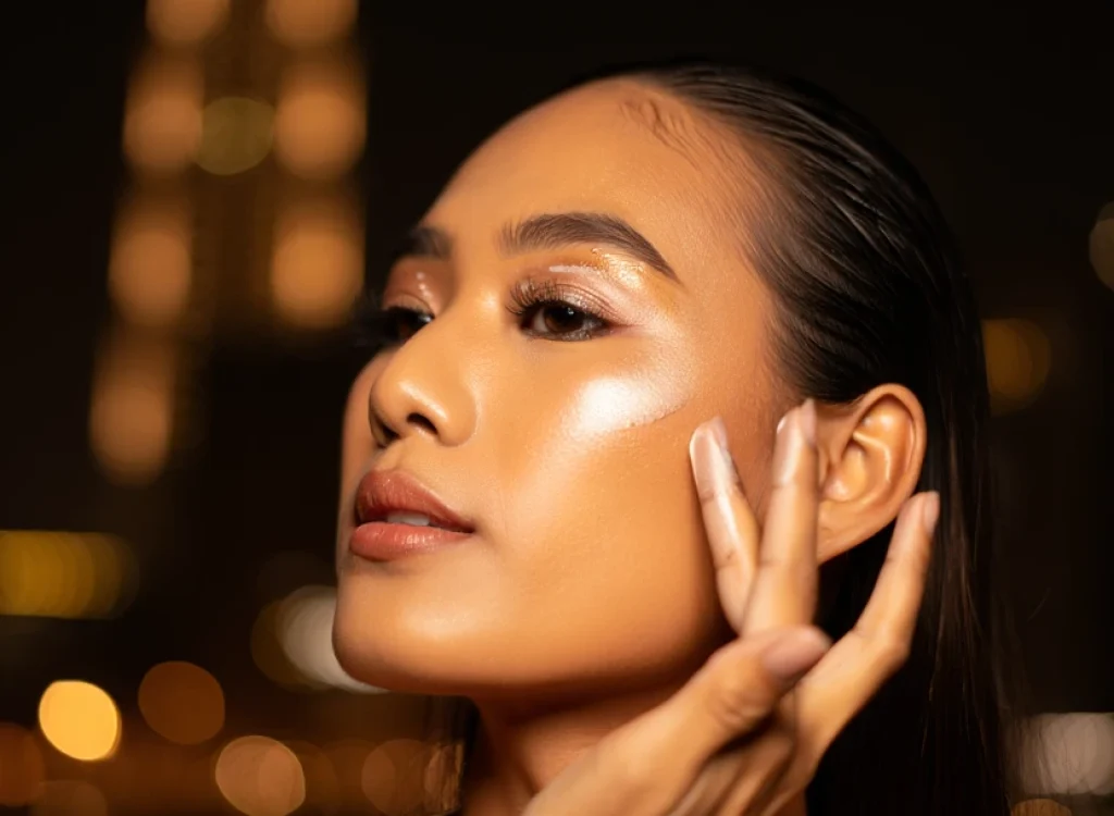 Woman applying highlighter on her cheekbones for a glowing Dubai glam look. ikmage name bana